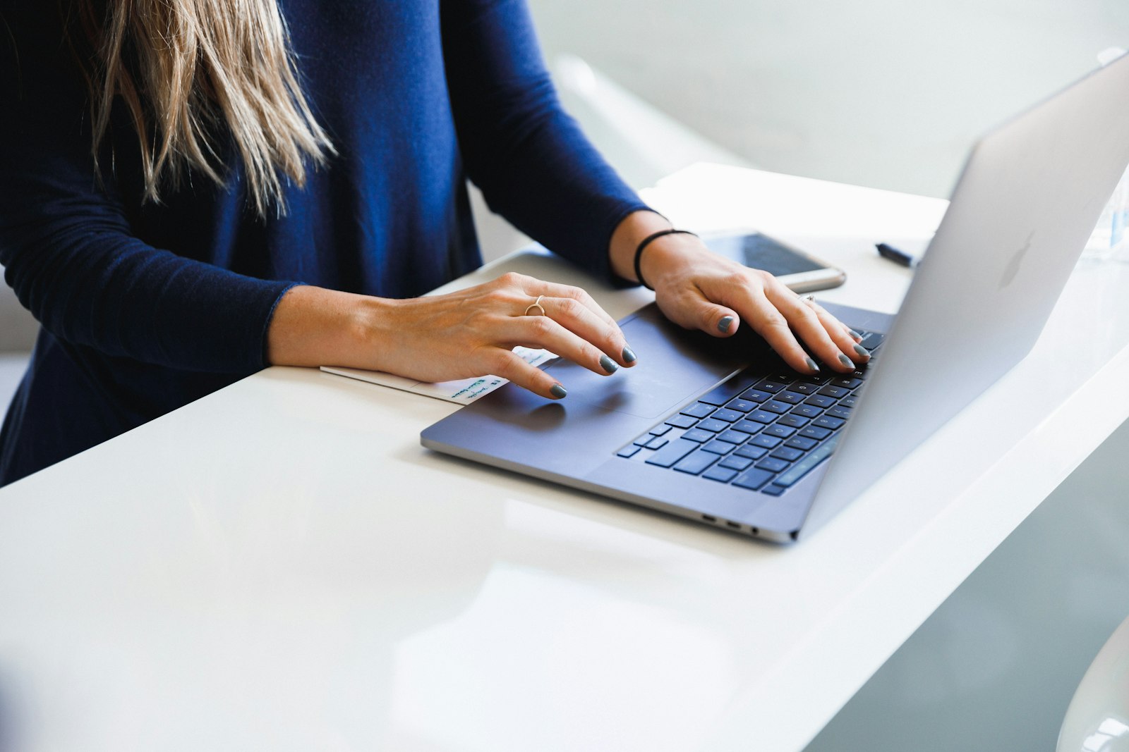 A woman typing on a laptop at a white desk